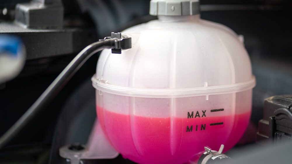 Close-up of a car’s coolant reservoir with antifreeze liquid during winter.